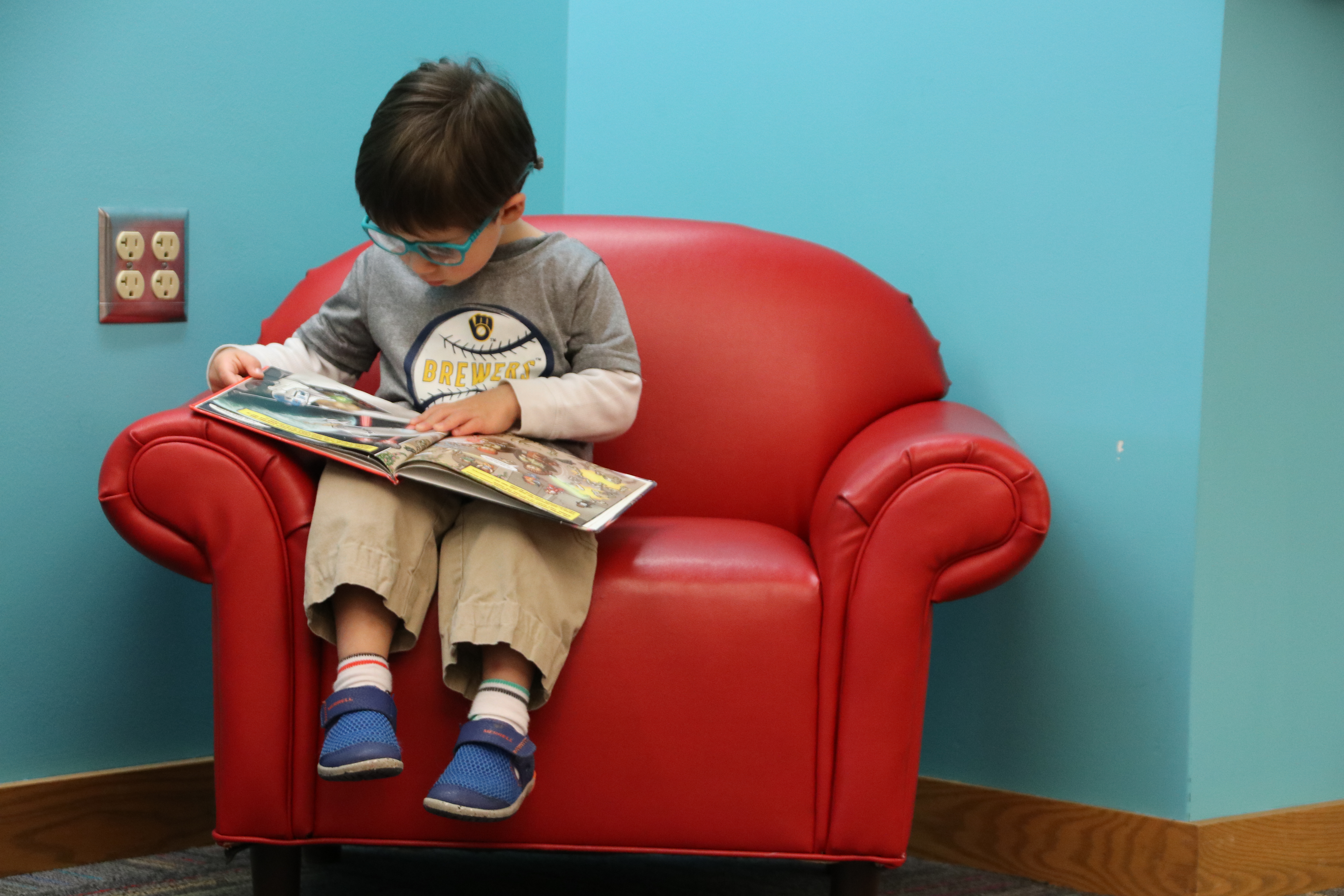 Child reading book in small red armchair