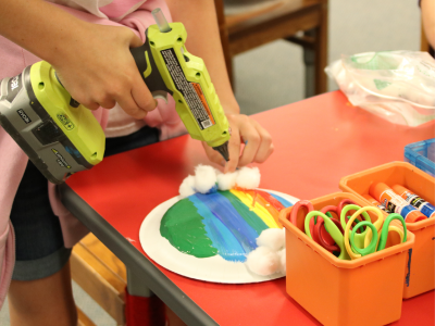 Person using hot glue to attach cotton balls to painted rainbow craft