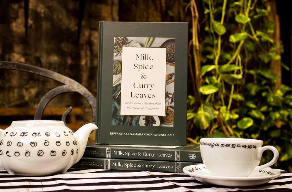Photo of the cookbook "Milk, Spice, and Curry Leaves" set on a table with a teapot and teacup