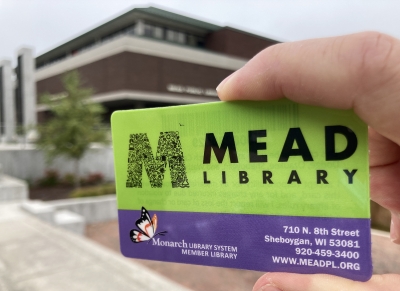 Hand holding purple and green Mead Library card with building in background